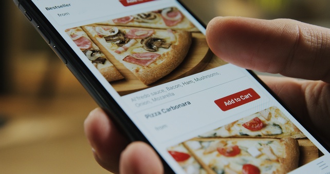 Une personne tient un téléphone dans la main tandis qu'elle commande une pizza en ligne.  